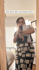 Mother taking a mirror selfie while holding her baby. The baby’s face is covered with a heart for privacy. A caption on the image reads “dirty mirror and a crazy amount of love.”