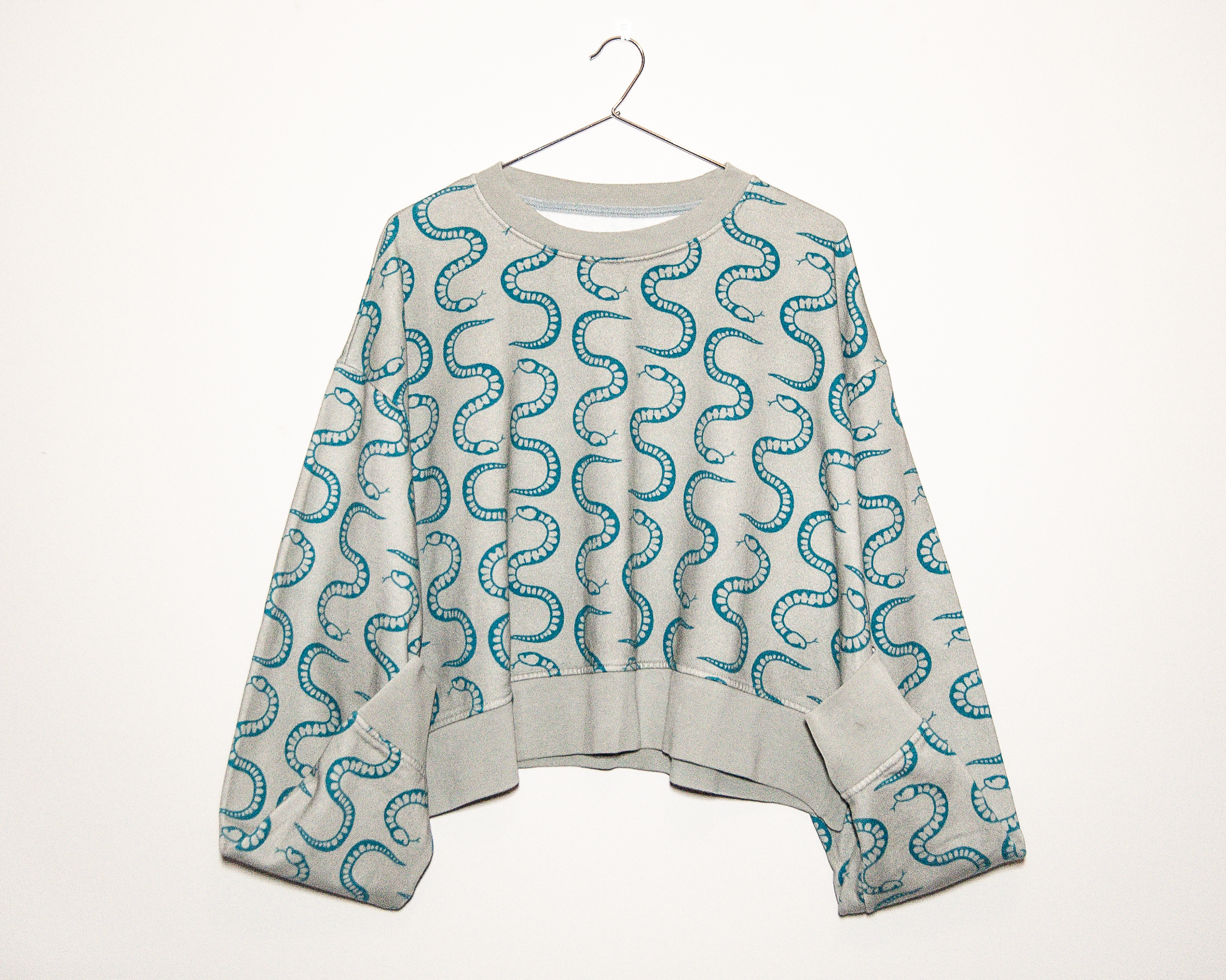 organic cotton women’s sweatshirt with teal snake print hanging on a white wall